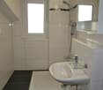 Bathroom: all white tiles, shower, sink, toilet, natural light from window