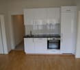 white cupboards, wooden floor, stainless steel oven, sink with faucet, black countertop