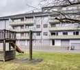 Multi-story apartment building, balconies, windows, slide, swings, garage doors, playground, tree