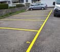 Large concrete parking lot with yellow parking spaces marked, building in the background, parked cars