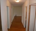 Empty hallway, wooden floor, white walls, white ceiling, a lamp hanging from the ceiling