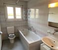 a bathroom with a white bathtub, white toilet, white sink, and a mirror with a light