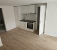 Empty kitchen with white cabinets, wooden floor, black countertop, sink, oven, and a door leading to the bathroom.
