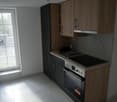 Modern kitchen with wooden cabinets, black appliances including a dishwasher, and a large window providing natural light