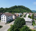 Aerial view of a residential area with several buildings, a parking lot, and a mountain in the background.