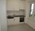 modern kitchen with white cabinets, black countertops, stainless steel sink, dishwasher, oven, and a window with a view