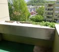 Balcony with green carpet, concrete railing, view of trees and buildings