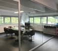 modern office room with glass walls, large windows, glass table, black chairs, plants, cabinets, printer