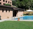 Swimming pool, brick building, green lawn, potted plants, umbrellas, tables and chairs