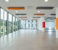 A spacious building hallway with large glass windows, tiled floor, tall columns, and bright ceiling lighting.