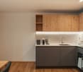 Modern kitchen with wooden cabinets, white countertops, and a wooden floor. Equipped with a sink, faucet, electric kettle, coffee machine, and various kitchen items.