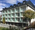 3-story apartment building with white exterior, glass balconies, and black roof dormers