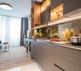 Modern kitchen with gray cabinets, wooden shelves, built-in appliances, and a Siemens dishwasher. The kitchen has a sleek and minimalist design with ample counter space and storage. The large windows provide natural light and a view of the living area.