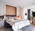 Spacious bedroom with wooden paneling, large bed, bedside tables, and a TV. The room has a cozy and modern feel with gray curtains and a rug on the floor.