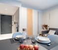 The image shows a modern and stylish open-plan living and dining area. The space features a gray sofa, a dining table with place settings, and a kitchen area with a dishwasher visible. The walls are painted in light colors, and the room has a mix of woode