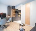 Modern kitchen with gray cabinets, wooden shelves, built-in appliances, and a dining area with a table and chairs