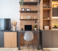 Desk with laptop, office chair, flat screen TV, books, shelves with photos and plants