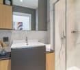 modern bathroom with marble tiles, white sink, shower, wooden cabinets, power outlet, vase with flowers