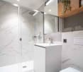 modern bathroom with white marble tiles, glass shower enclosure, white sink, white toilet, wooden cabinet with plant