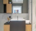modern bathroom with marble tiles, white sink, wooden cabinets, shower enclosure, mirror, power outlet, toilet paper holder