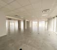 Large empty room with glass windows, gray tiled floor, pillars, circular black holes, high ceilings, view of the city