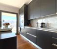 Modern kitchen with dark gray cabinets, stainless steel appliances, marble countertops, and a large window with a scenic view