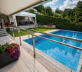 wooden deck, swimming pool, metal railing, flowers, plants, house in background