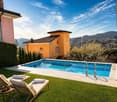 Swimming pool, lounge chairs, potted plants, green grass, yellow house, city view