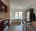 Kitchen with dining area, compact bedroom with bed, sliding doors leading to a balcony, white tiles, modern appliances, bed storage unit