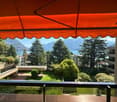 Balcony with panoramic view, trees, mountains and water, modern awning, garden with shrubs and lawn