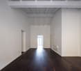 Empty room, white walls, wooden floor, white ceiling beams, doors on both sides, light coming from the end