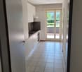 The image shows a modern kitchen with white cabinets and a black stove. The kitchen leads to a hallway with a tiled floor and a sliding glass door that opens to a balcony or terrace.