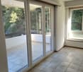 Empty room with sliding glass doors to balcony, tiled floor, white walls, and sunlight coming from the balcony.