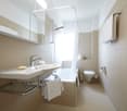 Spacious bathroom with white tiles, large vanity sink, mirror cabinet, shower, and toilet. Towels are provided.