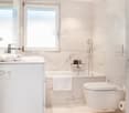 all white bathroom with bathtub, toilet, large mirror, white marble floors