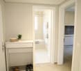 White walls, white tiles, storage with shoe rack, open doorway to bathroom