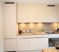 modern kitchen, white cabinets, under cabinet lighting, dishwasher, built-in microwave, oven, induction cooktop, wine bottle and glass