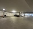 Large indoor parking garage with concrete floor, several parked cars, and overhead lighting.