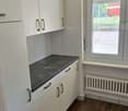 White cabinets, granite countertop, window with blinds, radiator