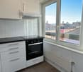 Kitchen with tile flooring, white cabinetry, black countertop, black oven, large window, and an exhaust hood