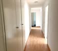 Empty hallway with white walls, wooden flooring, recessed ceiling light, doors to rooms.