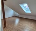 Empty room with wooden beams, wooden floor, white walls, a window, and a skylight