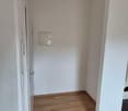 Wooden floor, white walls, single white door, single wall power outlet, single wooden beam