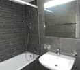 gray tile walls, white bathtub, white sink, silver faucet, mirror, shower head