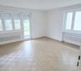 open room, wooden parquet floor, white walls, sliding glass door, two windows, white radiators