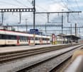 Train station with multiple tracks, train arriving, platform, overhead electrical wires, people waiting