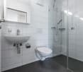 modern bathroom with white tiles, glass shower stall, white sink, toilet, and a mirror