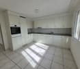 Fully equipped modern kitchen with white cabinetry, white tiled floor, oven, dishwasher, sink, countertops, lighting, and windows.
