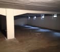 Empty parking lot, concrete floor, white walls, three small windows, central support pillar, overhead lighting.