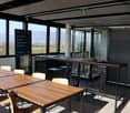 modern office room with large windows, wooden tables, chairs, black metal stools, glass door, black wall, advertisement board
